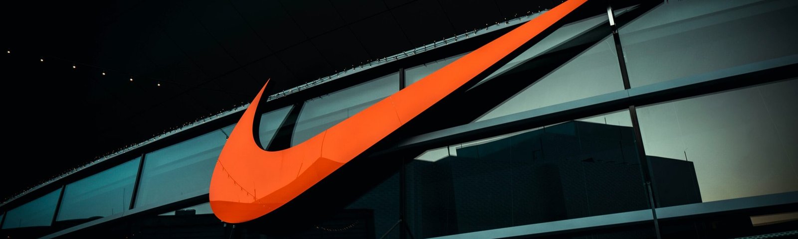 Large illuminated Nike swoosh logo on the exterior of a modern glass building, symbolizing the brand’s innovative approach and commitment to data-driven personalization in sportswear and customer experiences.